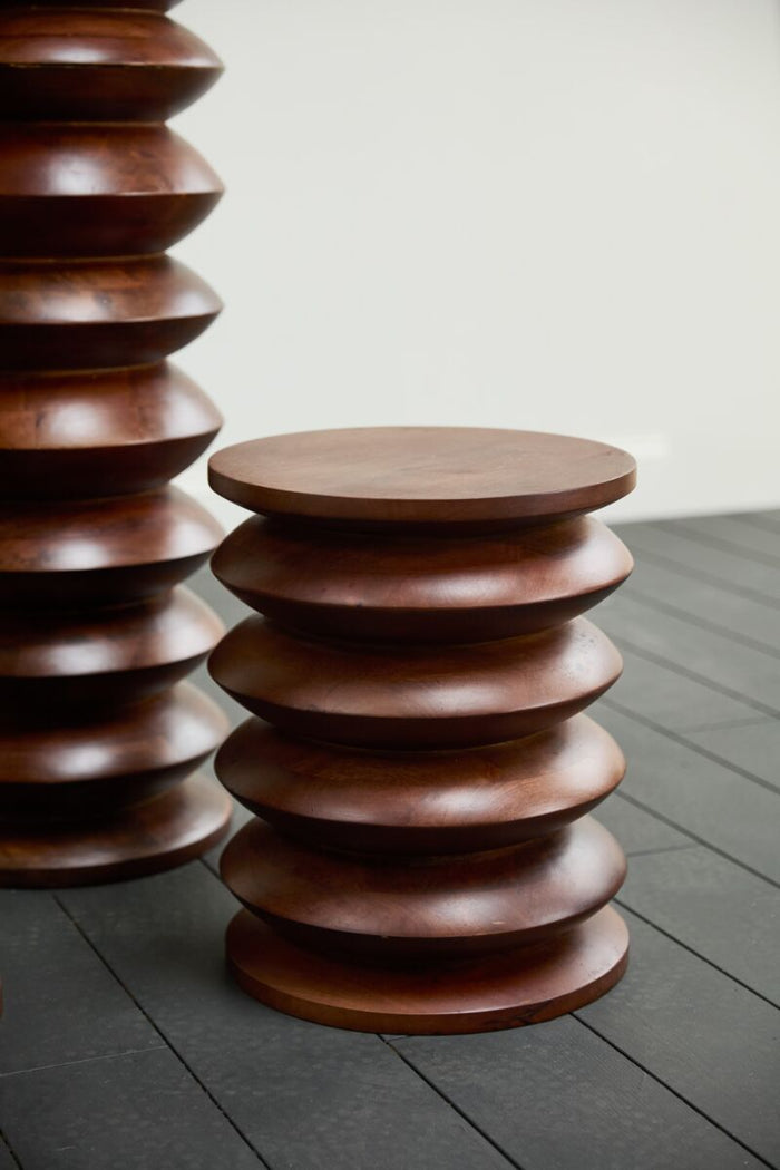 Stacked wooden tables on a gray floor with a neutral background