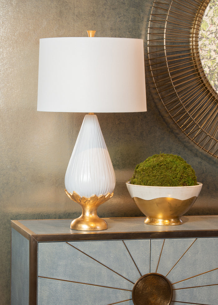 Decorative table lamp with white shade and gold base on a console table.