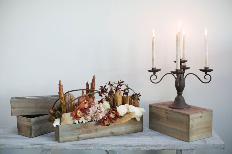 Decorative items including a wooden box with flowers, a basket with dried plants, and a candle holder on a white surface.