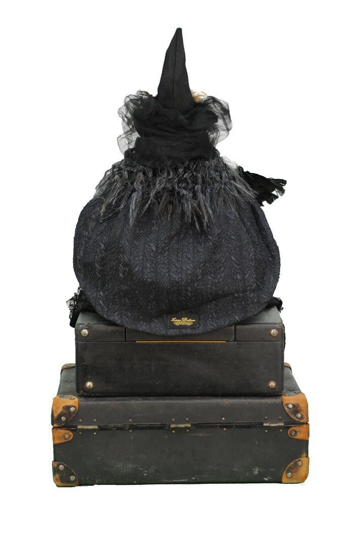 Black witch hat with decorative elements on top of vintage suitcases against a white background
