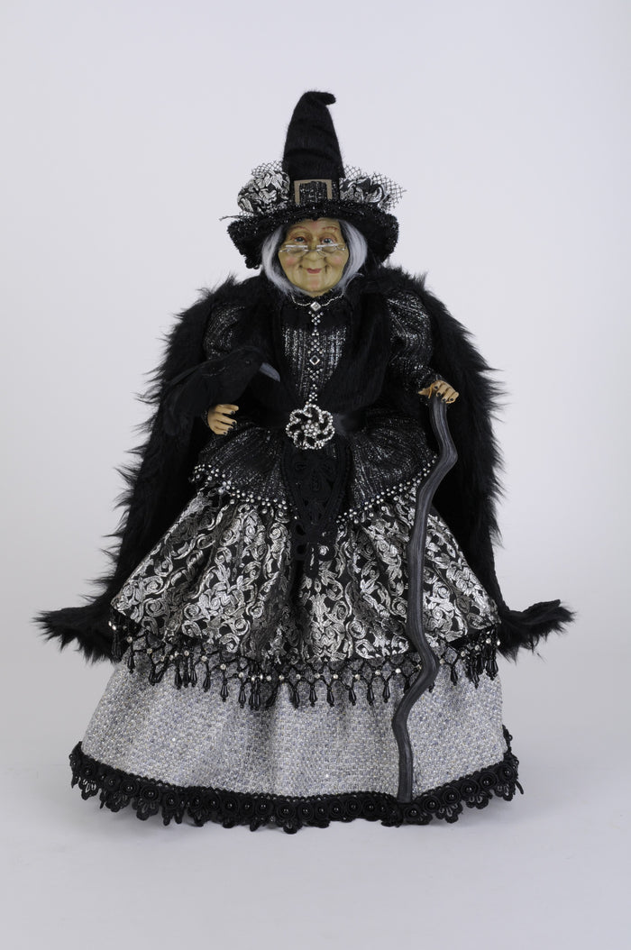 Decorative witch figurine with black fur, hat, and silver dress on a white background