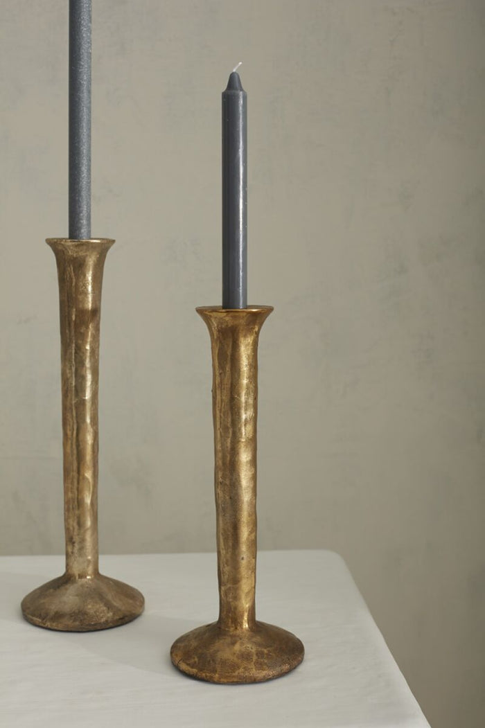 Two gold candle holders with black candles on a neutral background