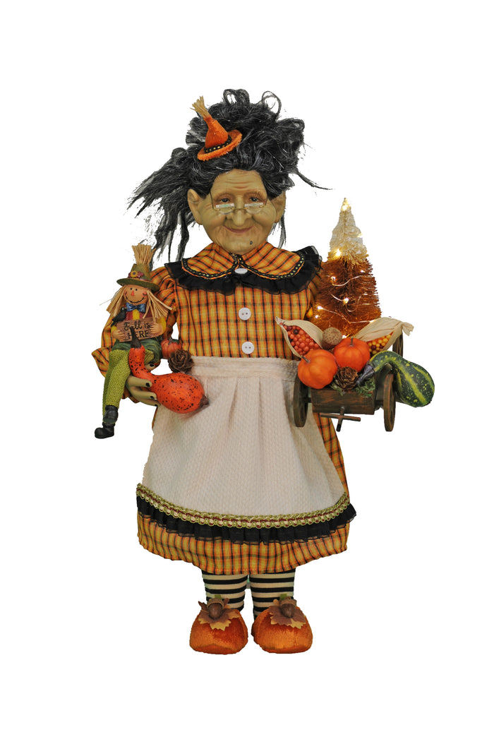 Decorative figurine of a witch holding pumpkins and a broom on a white background