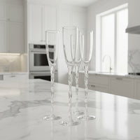 Set of four clear champagne flutes on a marble countertop in a modern kitchen.