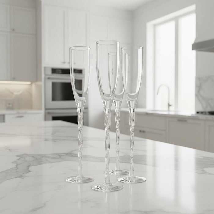 Set of four clear champagne flutes on a marble countertop in a modern kitchen.