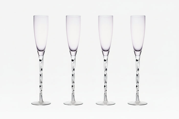 Set of four clear champagne flutes on a white background.
