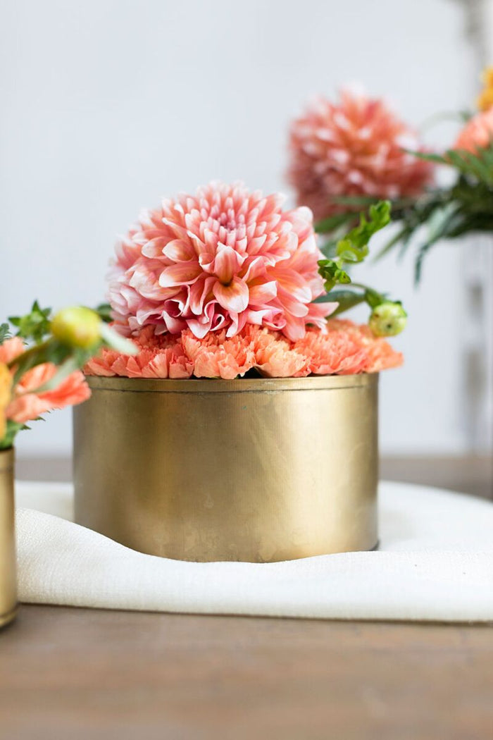 Pink flowers in a gold pot on a white surface with a blurred background