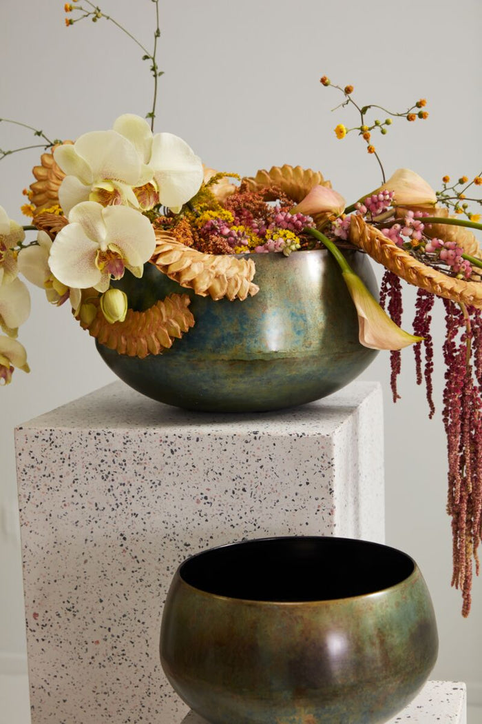 Decorative floral arrangement in a metallic bowl on a textured surface with a neutral background