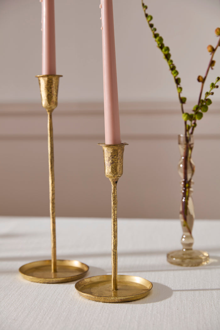 Two gold candle holders with pink candles on a white surface.