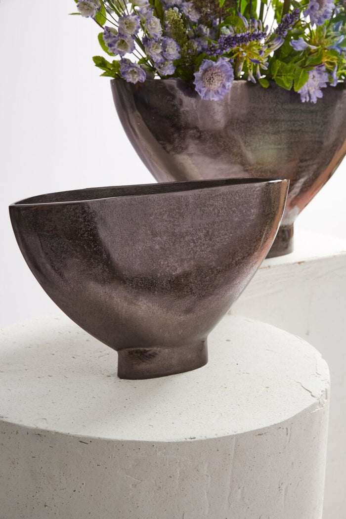 Two dark ceramic bowls with a floral arrangement on a white surface