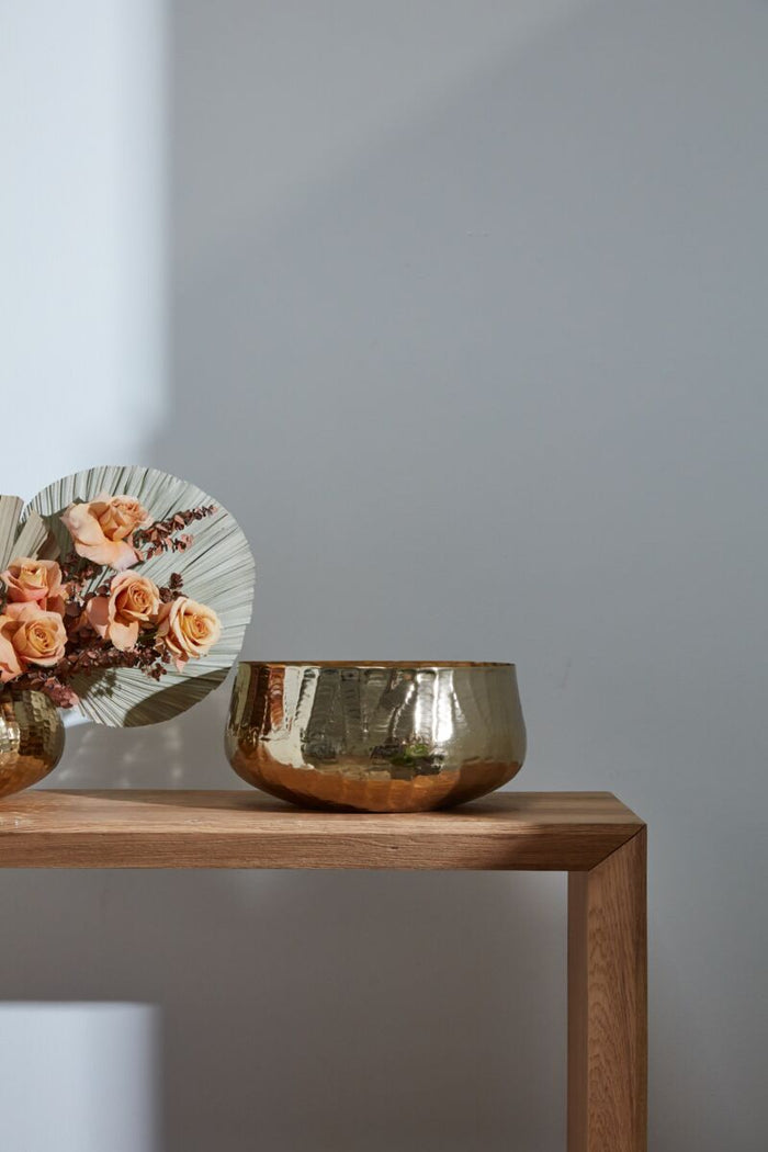 Decorative items including a metallic bowl and floral arrangement on a wooden shelf against a plain wall.