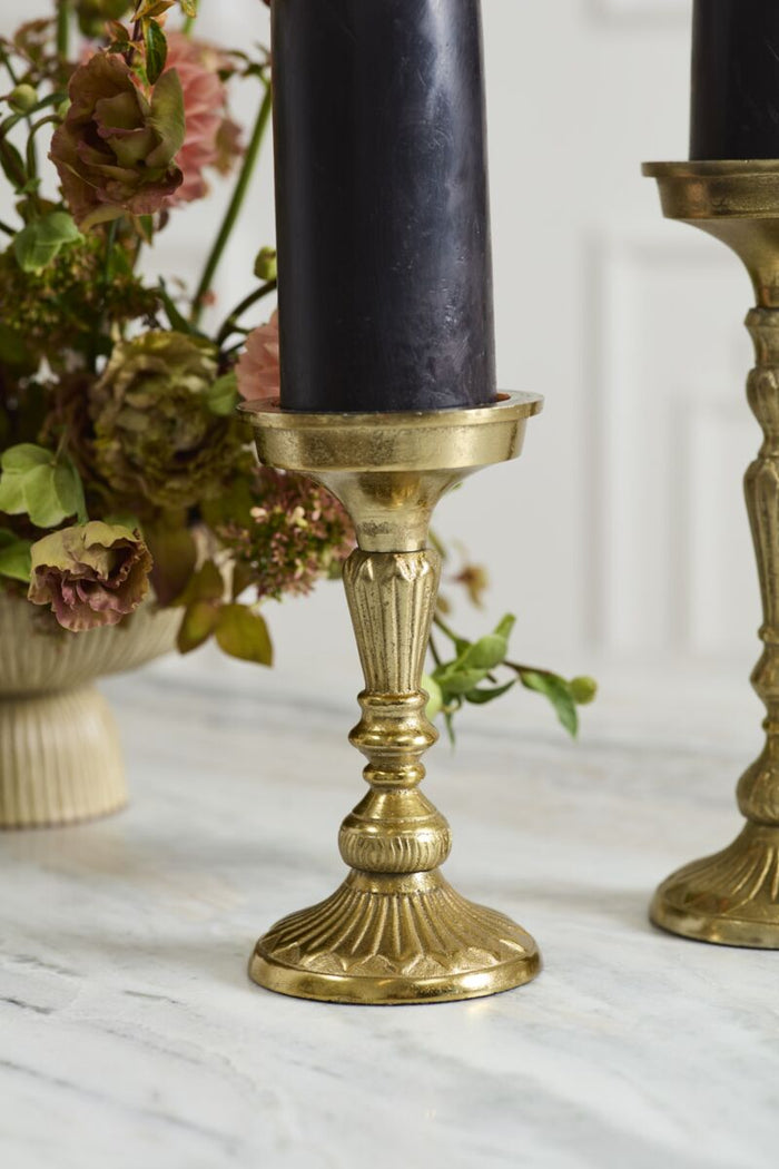 Gold candle holder with a black candle on a marble surface with flowers in the background