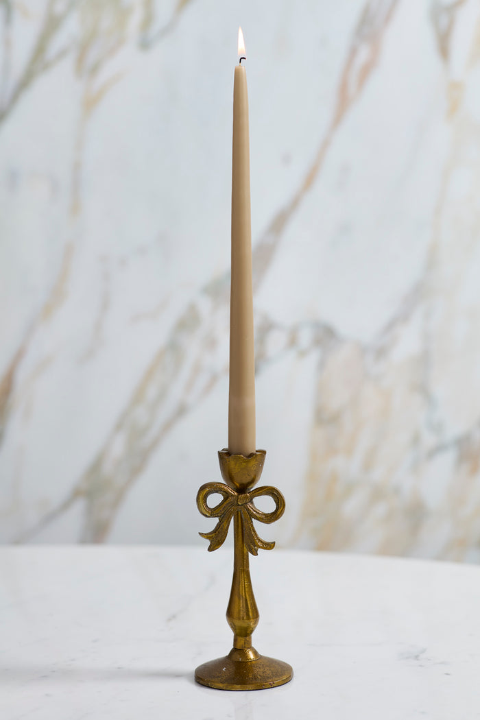 Brass candlestick holder with a lit candle against a blurred natural background