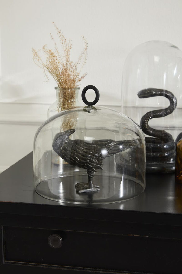 Decorative black bird sculpture under a glass dome on a dark surface.