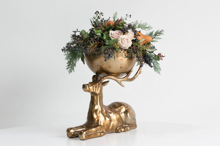 Decorative object with a gold deer figure holding a bowl of flowers on a white background