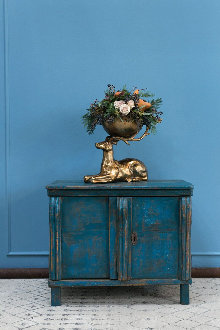 Decorative blue cabinet with a gold statue and floral arrangement against a blue wall.