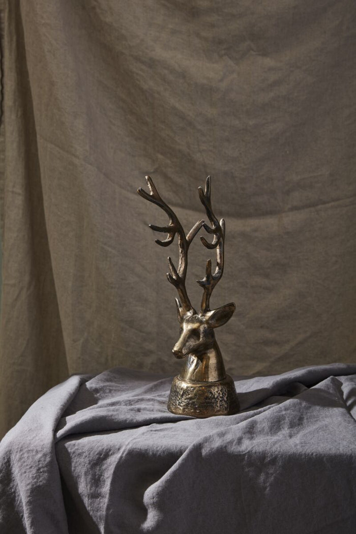 Bronze deer head sculpture on a textured surface with a neutral background