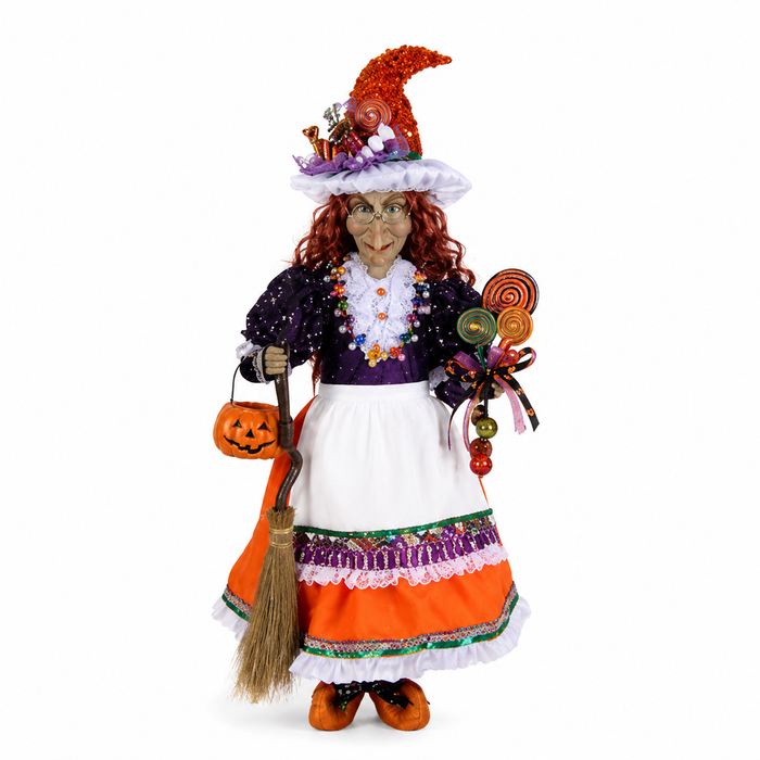 Halloween-themed doll with witch costume, broom, and candy on a white background