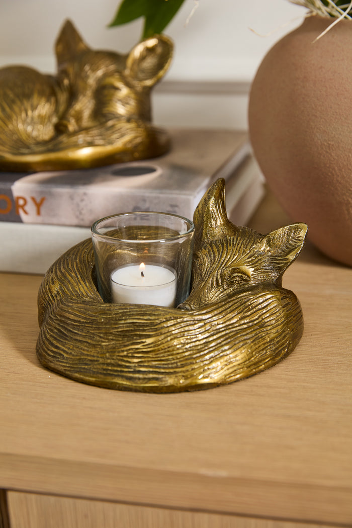 Gold fox-shaped candle holder with a candle on a wooden surface.
