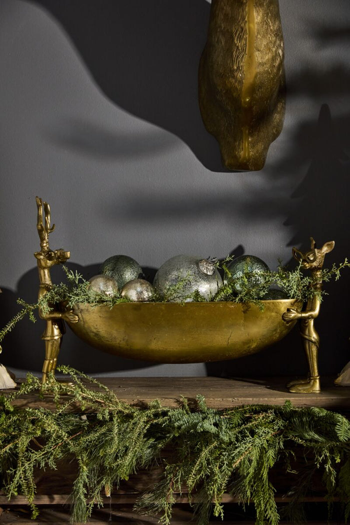 Decorative setup with a gold bowl, silver balls, and greenery on a dark background