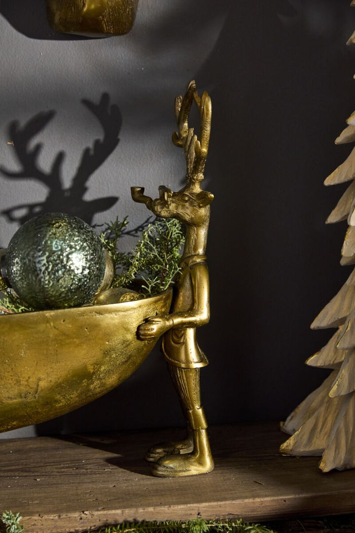 Gold figurine of a person with antlers holding a bowl with greenery against a dark background