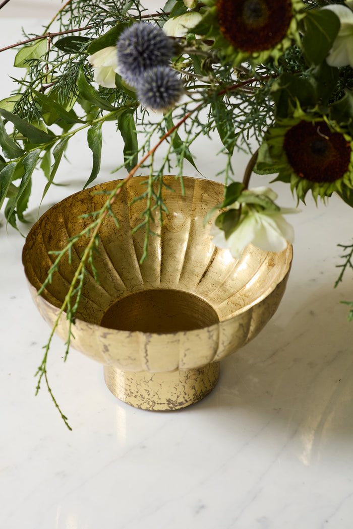 Gold decorative bowl with greenery on a marble surface