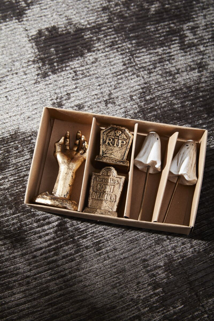 Decorative items including a hand, tombstone, and skull in a box on a textured surface.