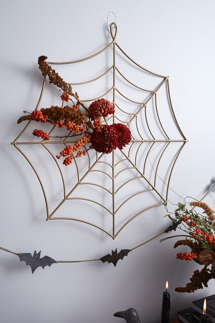 Decorative spider web with autumnal elements on a white wall.