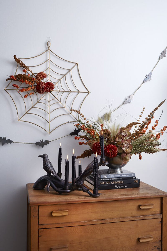 Halloween-themed decor with spider web, candles, and books on a wooden surface.