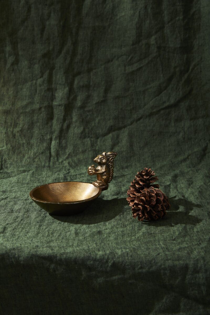 Bronze squirrel-shaped spoon rest with a pine cone on a green fabric background
