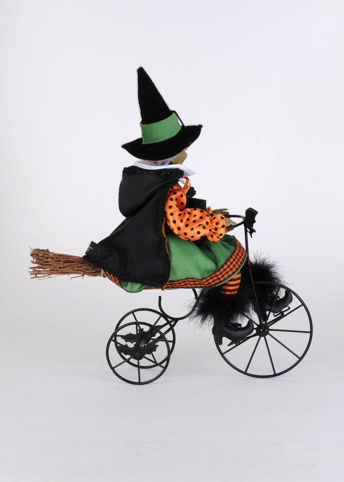 Halloween-themed witch figurine riding a tricycle on a white background
