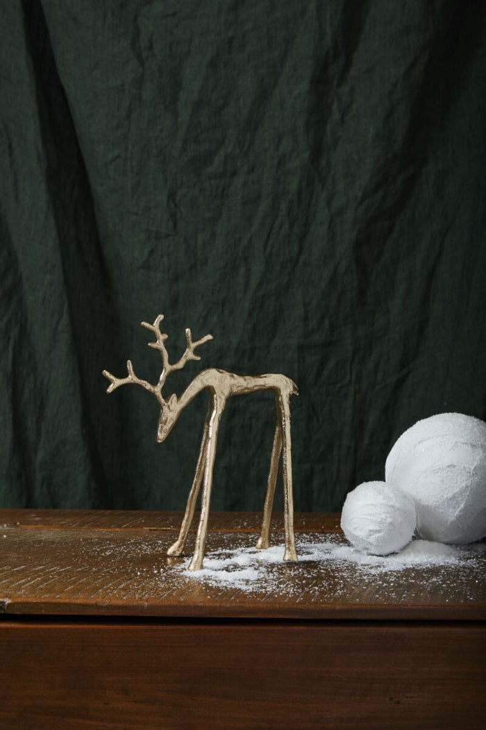 Decorative reindeer figure on a wooden surface with white balls and dark green curtain background