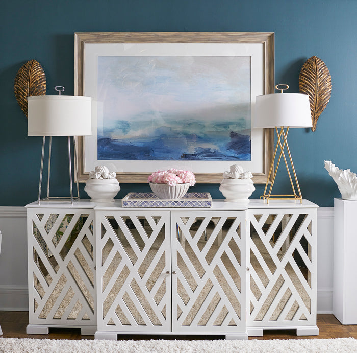 Decorative console table with lamps, artwork, and decorative items against a blue wall.