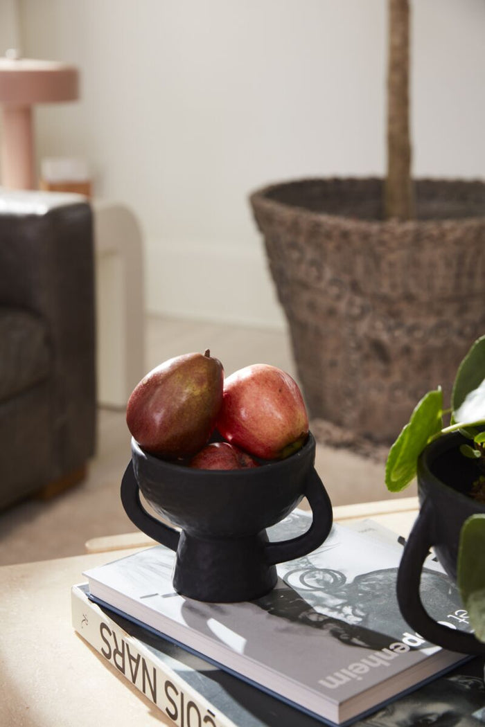 Black decorative bowl with pomegranates on a book in a home setting