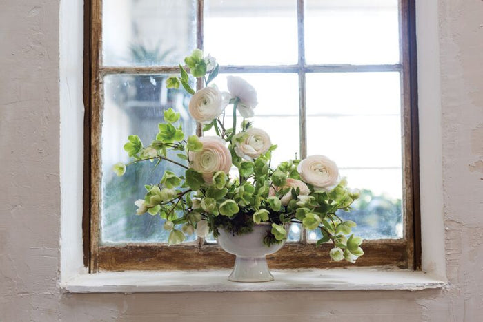 Floral arrangement in a white vase on a windowsill with a blurred outdoor background