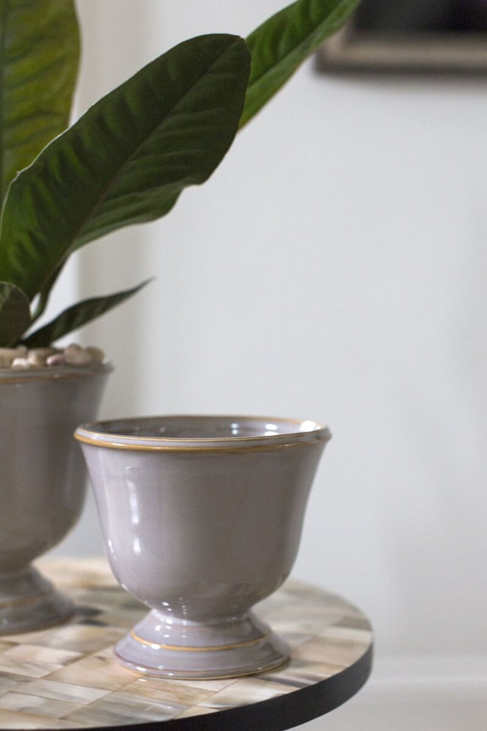 Gray ceramic planter on a marble surface with a plant in the background