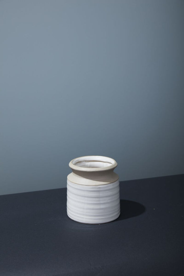 White ceramic vase with ribbed texture on a dark surface and gray background
