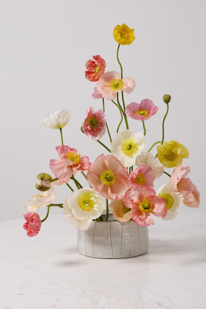 Bouquet of pink, yellow, and white flowers in a textured pot on a light background