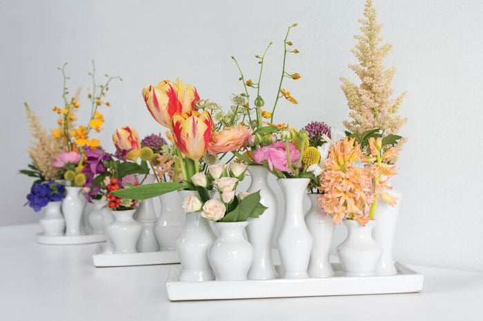 Assorted floral arrangements in white vases on a white surface with a light gray background