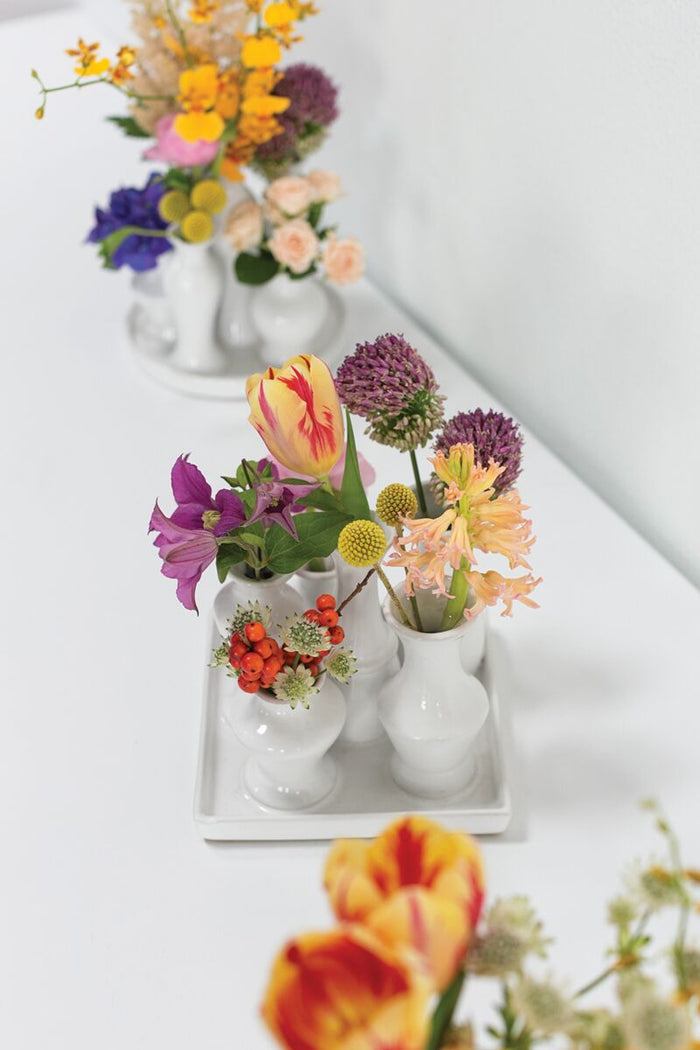 Colorful flowers in small white vases on a white surface