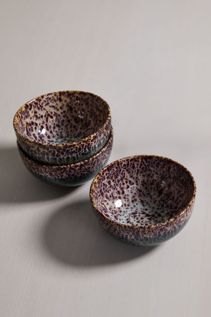 Set of four speckled brown and cream glazed ceramic bowls, shallow, stacked one inside another on a neutral surface.