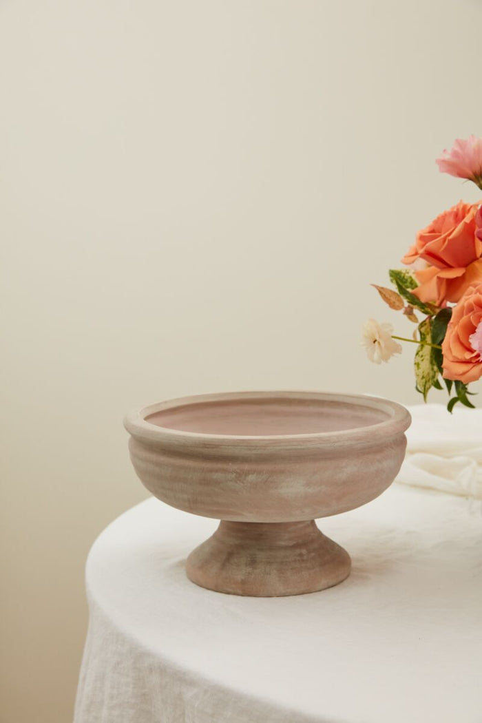 Terracotta bowl on a white surface with flowers in the background
