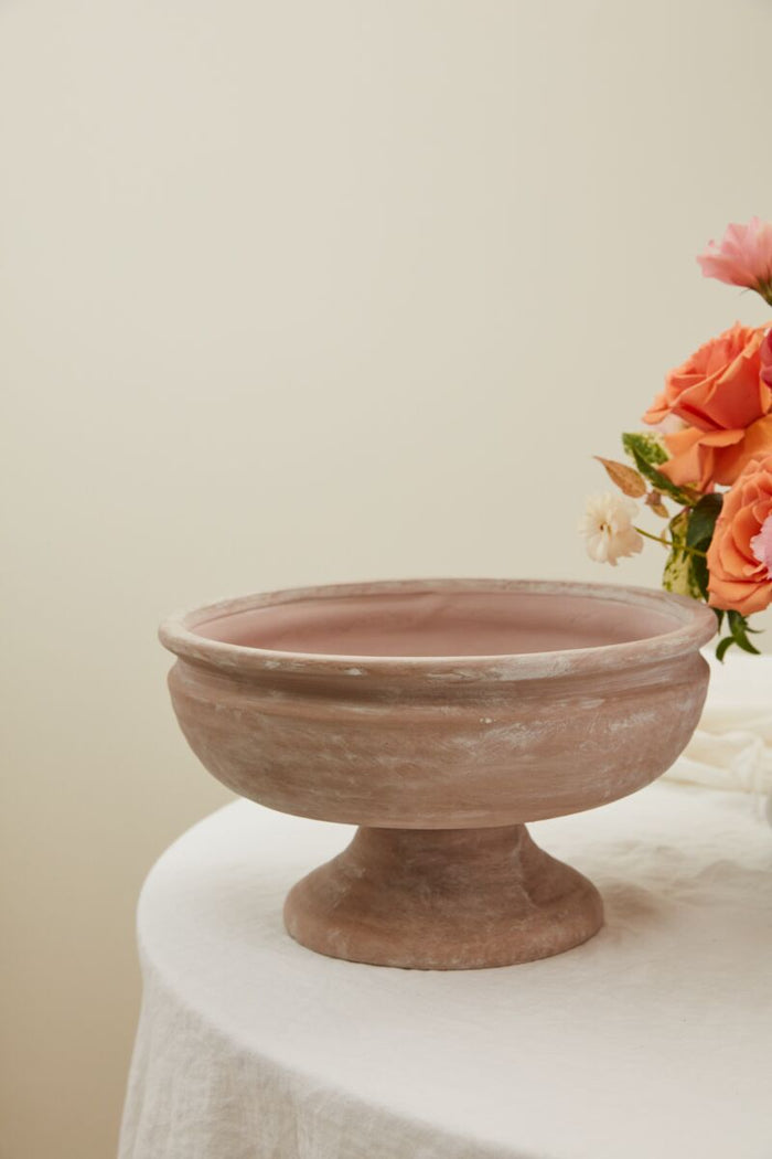 Terracotta bowl on a white surface with flowers in the background