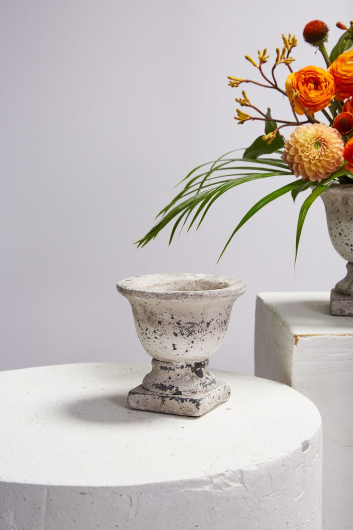 Concrete vase on a white surface with a bouquet of flowers in the background