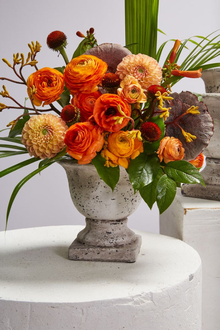Floral arrangement in a concrete urn on a white surface with a light gray background