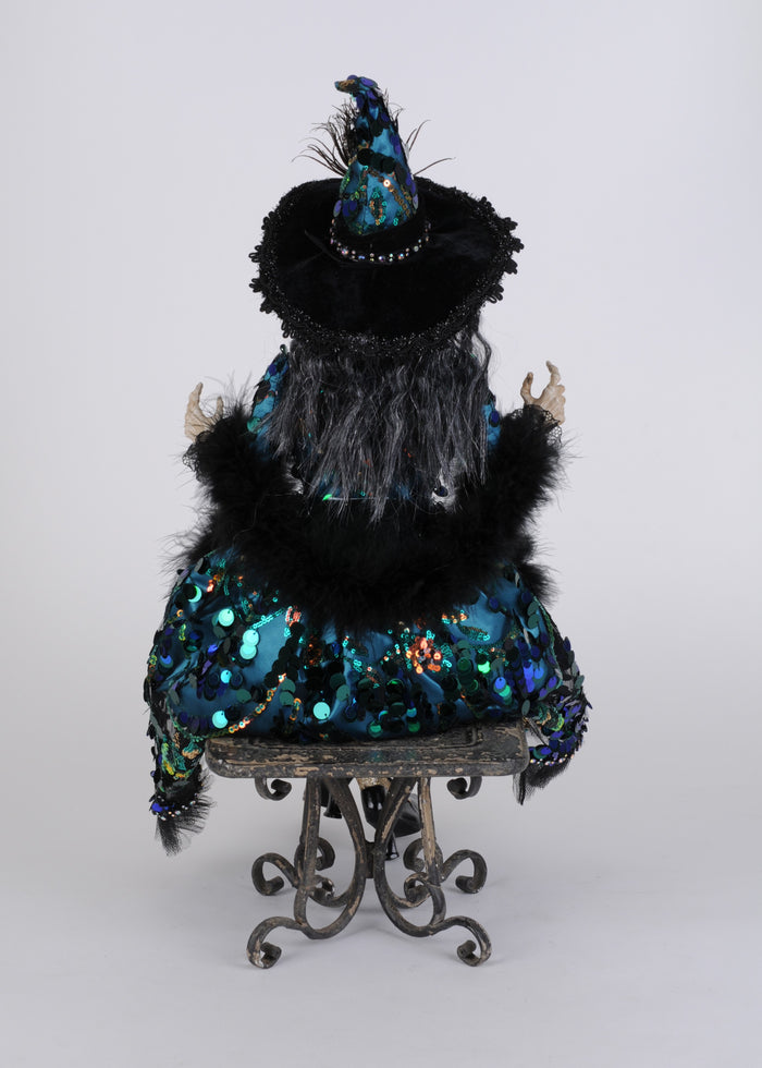 Decorative figure with black fur, blue sequin dress, and pointed hat on a white background