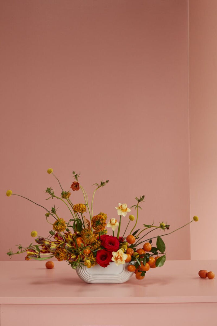 Floral arrangement in a white vase on a pink surface with a pink background