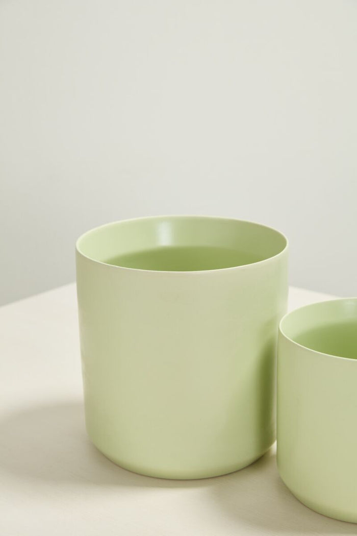 Two light green ceramic pots on a white surface with a light gray background