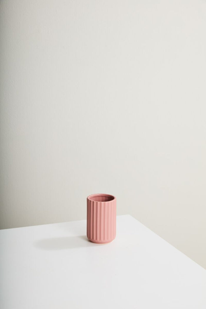 Pink textured vase on a white surface with a light gray background