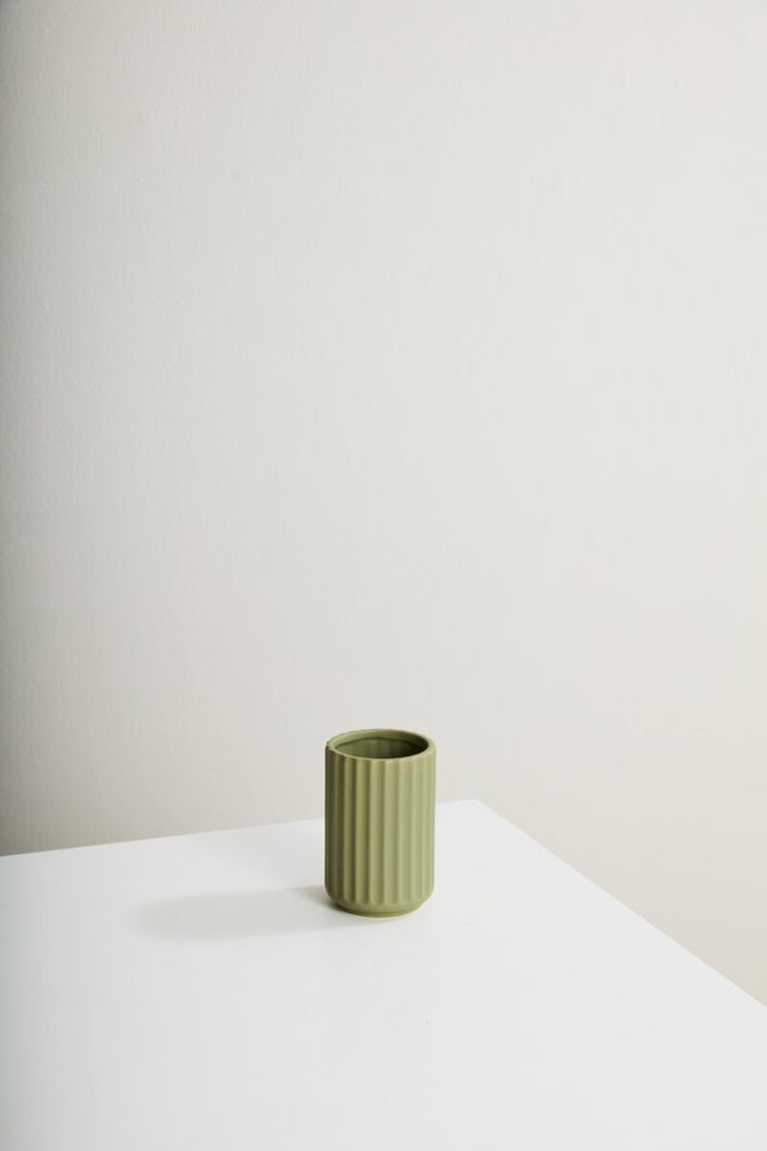 Green ceramic vase on a white surface with a plain background